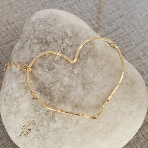 Puede incluir: Un collar dorado con un colgante de coraz&oacute;n martillado. El coraz&oacute;n est&aacute; abierto y tiene una cadena delicada.