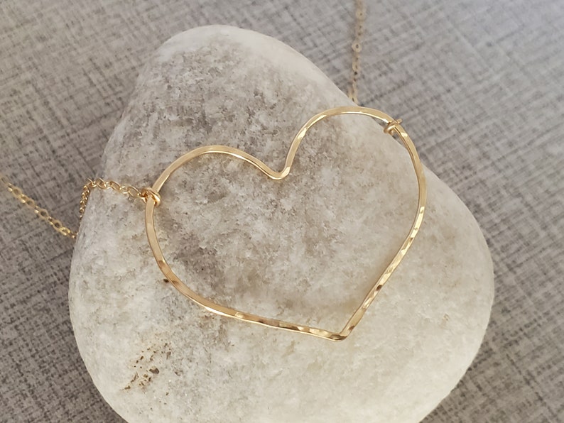 Puede incluir: Un collar dorado con un colgante de coraz&oacute;n martillado. El coraz&oacute;n est&aacute; abierto y tiene una cadena delicada.