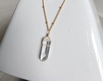 May include: A gold chain necklace with a clear quartz crystal pendant. The crystal is faceted and has a pointed tip.