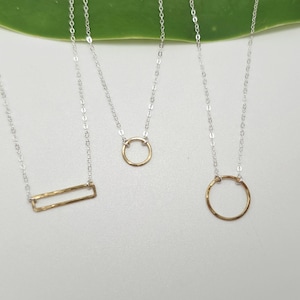May include: Three necklaces featuring thin silver chains. One necklace has a horizontal gold-toned rectangular pendant, while the other two necklaces feature gold-toned circular pendants of different sizes, all with a textured, hammered finish.