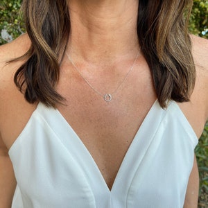 May include: A silver necklace with a simple circle pendant. The necklace is worn by a person with long brown hair and a white top.