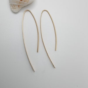 Pode incluir: Um par de brincos de metal em tom dourado com um design de fio longo, fino e em forma de U. Os brincos t&ecirc;m um acabamento liso e polido e uma silhueta curva e alongada que termina em ponta nas extremidades inferiores da estrutura.