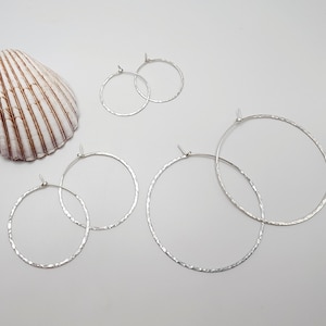 May include: Three pairs of silver hoop earrings of varying sizes. The earrings are hammered and have a textured finish.