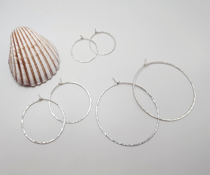 May include: Three pairs of silver hoop earrings of varying sizes. The earrings are hammered and have a textured finish.