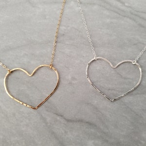 Puede incluir: Dos delicados collares con colgantes de coraz&oacute;n martillados. Un collar es dorado y el otro es plateado.