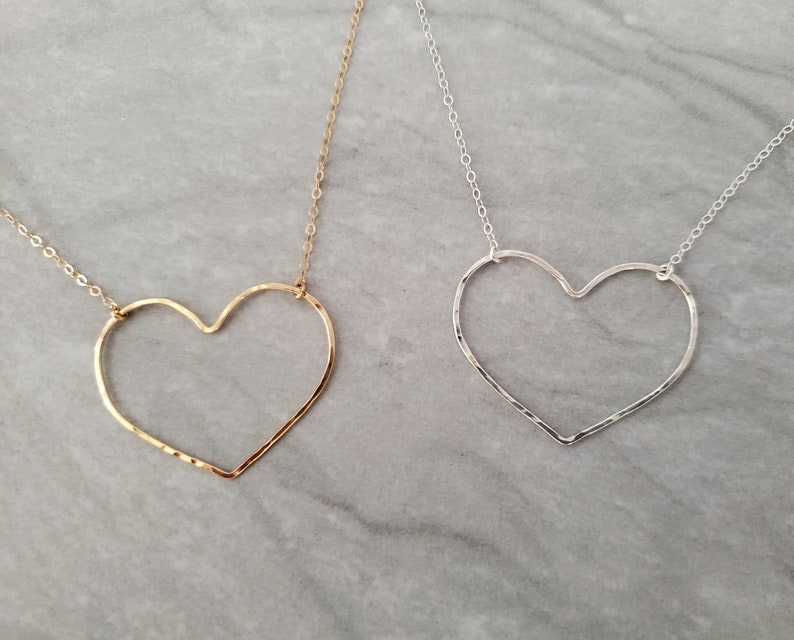 Puede incluir: Dos delicados collares con colgantes de coraz&oacute;n martillados. Un collar es dorado y el otro es plateado.