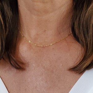May include: A close-up of a woman wearing a simple gold chain necklace. The chain is delicate and has a subtle shine.