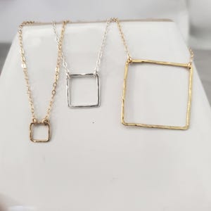 May include: Three necklaces featuring square pendants on delicate chains. One small gold square pendant on a gold chain, one medium silver square pendant on a silver chain, and one large gold square pendant on a gold chain. Each pendant has a hammered texture.