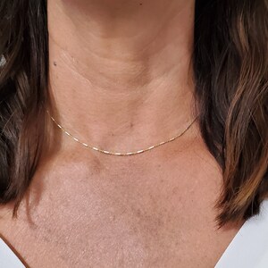 May include: A delicate gold chain necklace worn by a person with brown hair. The chain is thin and has a simple design.