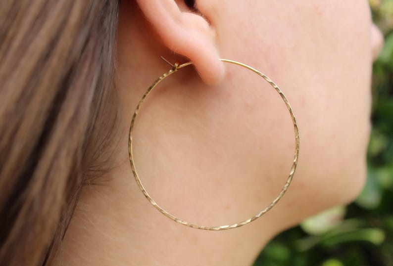 May include: Gold hoop earrings with a textured finish. The earrings are large and circular.