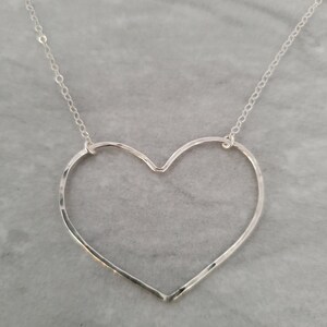 Puede incluir: Un collar de plata con un colgante de coraz&oacute;n martillado. El coraz&oacute;n est&aacute; abierto y tiene una cadena delicada.