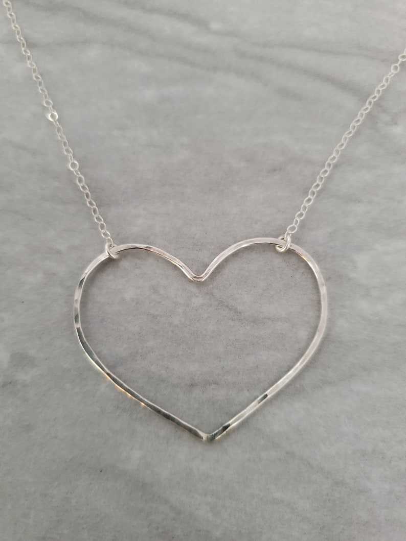 Puede incluir: Un collar de plata con un colgante de coraz&oacute;n martillado. El coraz&oacute;n est&aacute; abierto y tiene una cadena delicada.