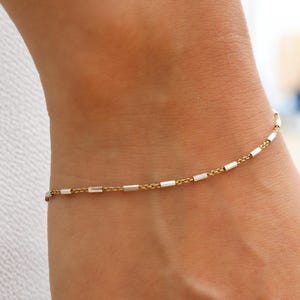 May include: A delicate gold chain bracelet with alternating gold and silver rectangular links.
