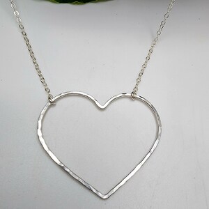 Puede incluir: Un collar de plata con un colgante de coraz&oacute;n martillado. El coraz&oacute;n est&aacute; abierto y tiene una cadena delicada.