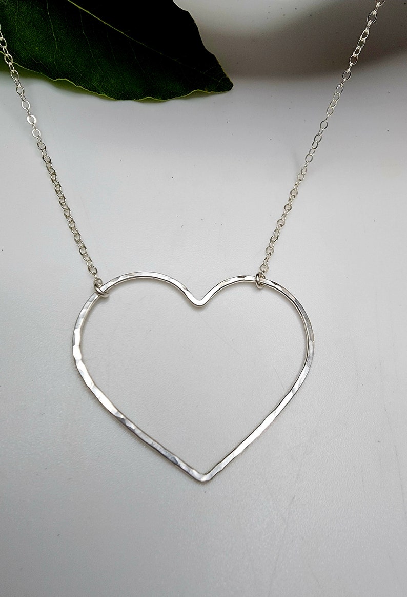 Puede incluir: Un collar de plata con un colgante de coraz&oacute;n martillado. El coraz&oacute;n est&aacute; abierto y tiene una cadena delicada.