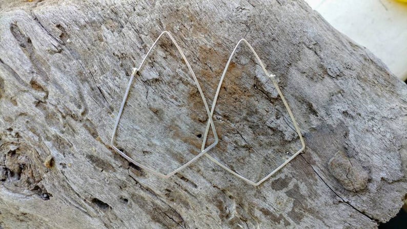 May include: A pair of silver geometric hoop earrings with a diamond shape. The earrings are made of thin wire and are lightweight.
