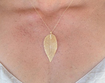 Könnte beinhalten: Eine goldene Halskette mit einer zarten Kette und einem großen, detaillierten Blattanhänger.