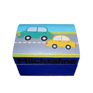 May include: A blue wooden box with a painted design of two cars on a road. The box has the text "Milchzähne" on the front.