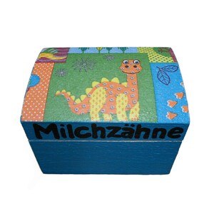 May include: A blue wooden box with a colorful dinosaur design and the text "Milchzähne" on the front.