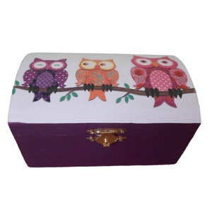 Peut inclure: Une boîte en bois violette avec un couvercle à charnières et un loquet doré. Le couvercle présente un fond blanc avec trois hiboux colorés perchés sur une branche.
