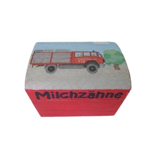 May include: Red wooden box with a fire truck illustration on the lid and the text "Milchzähne" on the front.