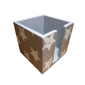Peut inclure: Un porte-serviettes en bois gris avec un motif d'étoiles blanches. Le porte-serviettes a une forme rectangulaire avec une ouverture sur un côté pour les serviettes.