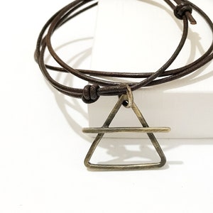 Może przedstawiać: Brązowy skórzany sznurek z naszyjnikiem z trójkątnym zawieszką z mosiądzu z poziomą linią w środku.