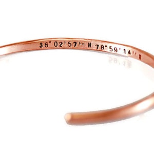 Op de afbeelding: Een roségouden metalen armband met de coördinaten "36° 02' 57" N 78° 59' 14" W" gegraveerd aan de binnenkant.