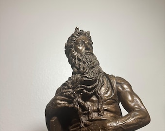 May include: A bronze sculpture of a seated figure with a long beard and curly hair. The figure is wearing draped clothing and has a serious expression. The sculpture is detailed and appears to be an antique.