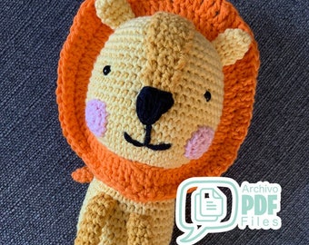 Puede incluir: Un juguete de peluche de león tejido a crochet con un cuerpo amarillo, una melena naranja y ojos negros. El juguete está sentado sobre una superficie de tela gris. El texto "Archivo PDF Files" es visible en la esquina inferior derecha de la imagen.