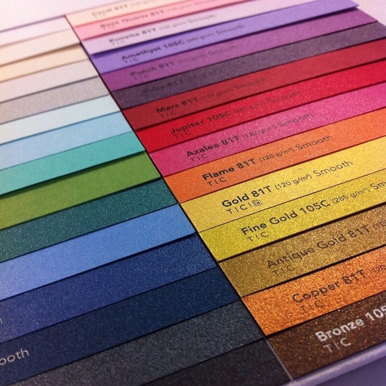 May include: A close-up of a color chart showing different shades of paper. The chart includes colors like amethyst, mars, jupiter, azalea, flame, gold, fine gold, antique gold, copper, and bronze. Each color is labeled with the name and weight of the paper.