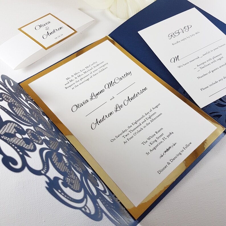 May include: A navy blue and gold wedding invitation with a laser-cut design. The invitation features the names Olivia Lynne McCarthy and Andrew Lee Anderson, the date and time of the wedding, and the location. The RSVP card is also included.