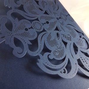 May include: A navy blue laser cut card with a delicate floral design. The intricate pattern features swirls, leaves, and dots.