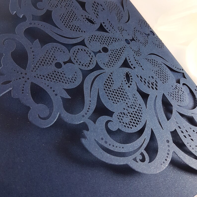May include: A navy blue laser cut card with a delicate floral design. The intricate pattern features swirls, leaves, and dots.