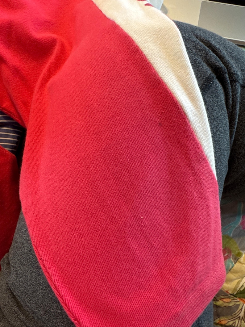 May include: A knit garment featuring a vibrant red section adjacent to a solid white stripe. The fabric displays a fine, consistent texture throughout the red and white panels, with a visible seam line running along the edge of the red fabric.