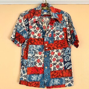 May include: Short-sleeved button-down shirt with a patchwork design. The shirt features a mix of red, white, and blue floral and geometric patterns. The shirt is hanging on a metal hanger.