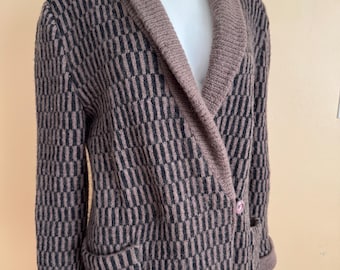 May include: A long brown and black patterned cardigan with a shawl collar and two front pockets. The cardigan has a single pink button closure and brown cuffs. The pattern is a repeating vertical design.
