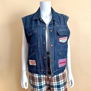 May include: A blue denim vest with a collar and button closure. The vest has several patches sewn on the front, including "Racing Team", "Honda 450", and "This is Honda Cowboy".