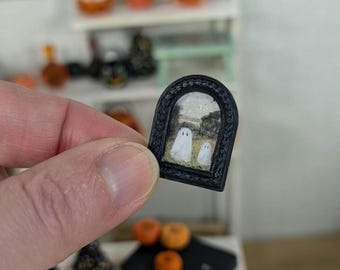 Może przedstawiać: Miniaturowa czarna ramka do obrazu z łukowatym górnym brzegiem. Ramka zawiera wydrukowany obraz dwóch białych duchów w krajobrazie.