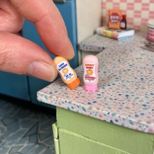 May include: Two miniature bottles of sunscreen. One is orange and says "Sun Screen SPF 50". The other is pink and says "Sunny Baby 50 Sunscreen".