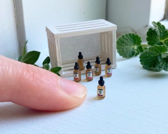 Può includere: Piccole bottiglie di vetro con contagocce neri, disposte vicino a una piccola cassa di legno. Ogni bottiglia ha un'etichetta con un disegno di foglia verde. Le bottiglie contengono un liquido ambrato chiaro.
