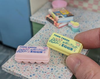 May include: Two miniature cartons of eggs, one pink and one yellow, both with the text "Farm Fresh Eggs" and a picture of chickens.