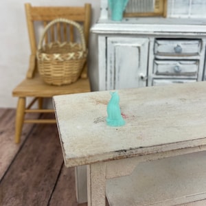 May include: A small, light blue figurine of a cat sitting on a white wooden table.