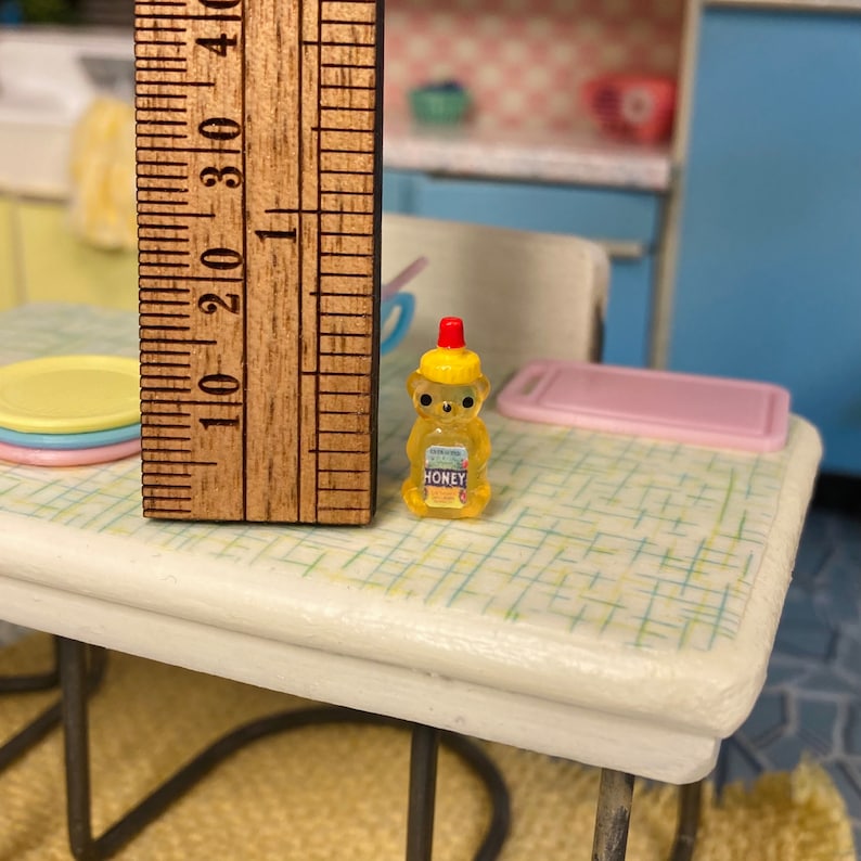 May include: A miniature yellow bear-shaped honey bottle with a red lid and a label that says "HONEY".
