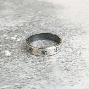 May include: A silver band ring with a textured surface and paw print designs around the band.