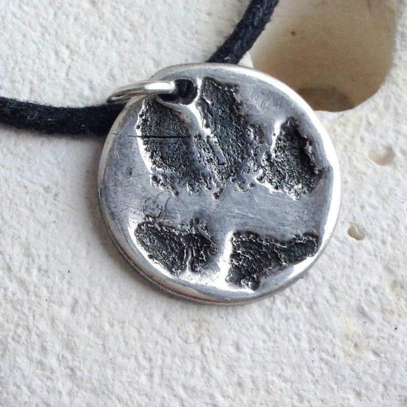 May include: A silver pendant with a textured paw print design. The pendant is attached to a black cord.