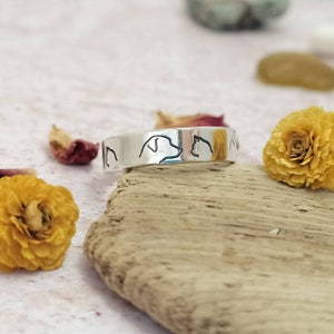 May include: A silver ring with a design of a dog and cat facing each other. The ring is on a piece of driftwood.