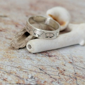 May include: A silver ring with a design of farm animals, including a cow, sheep, and pig, around the band.