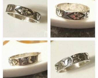 May include: Four silver rings with a floral design. The rings are on a white surface.