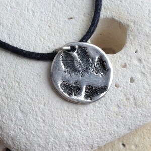 May include: A silver necklace with a round pendant featuring a detailed paw print design. The necklace is on a black cord.